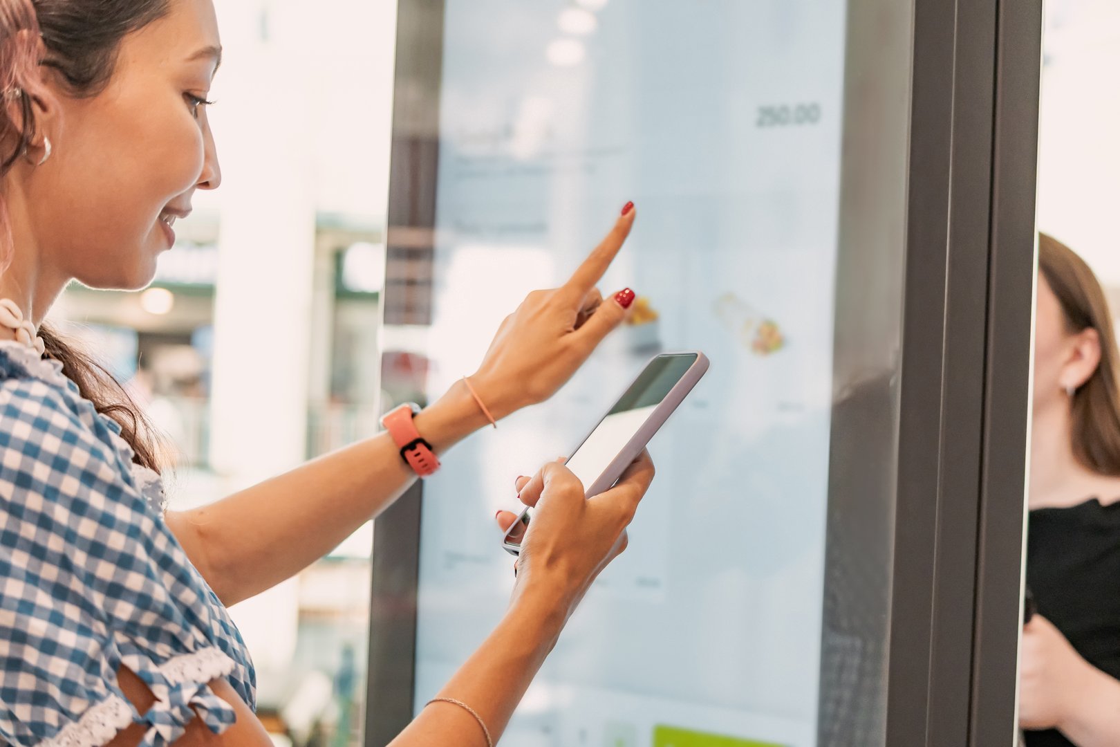 Customer using smartphone and interactive self ordering kiosk