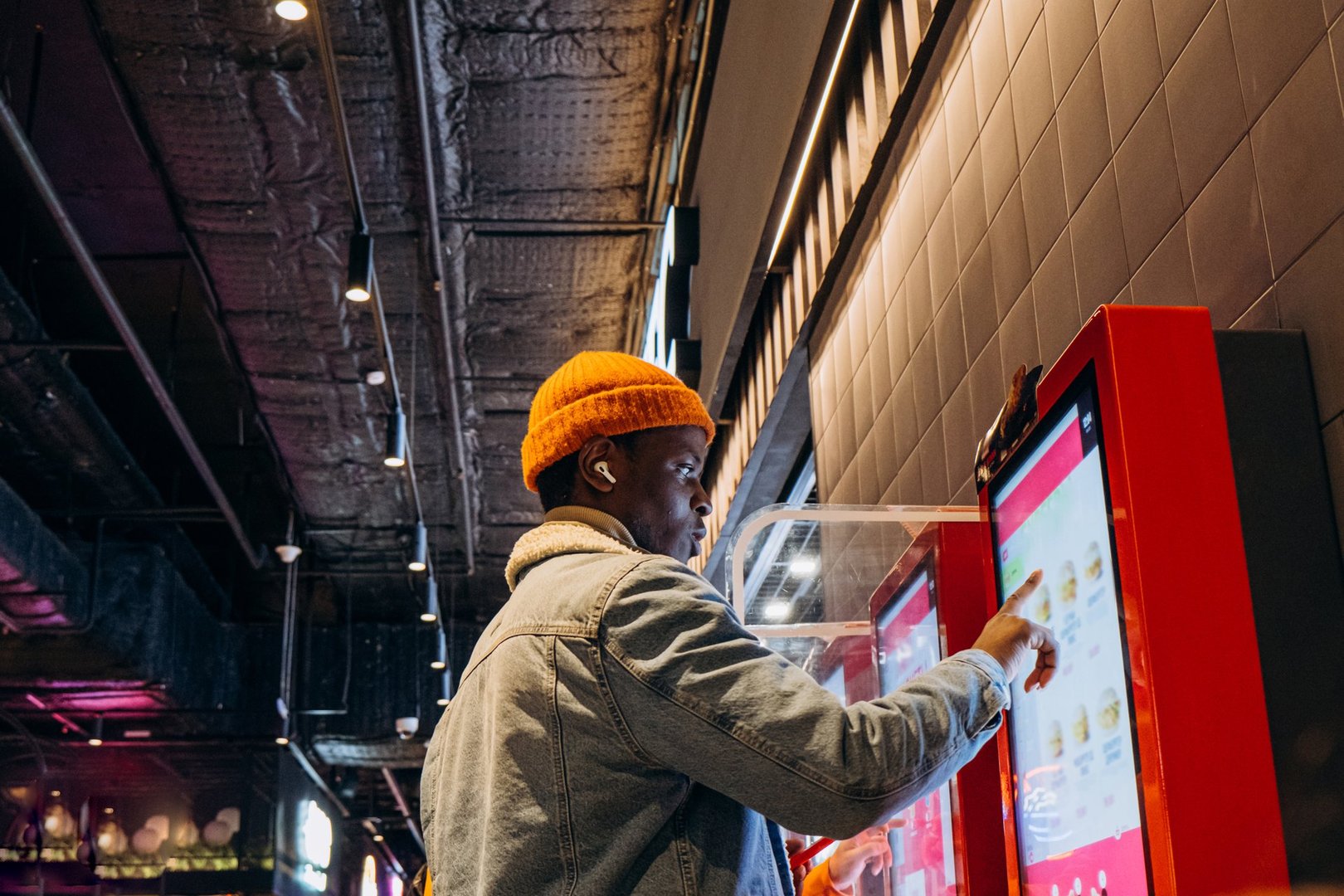 Smiling man uses self-service kiosk to order snack in cafe